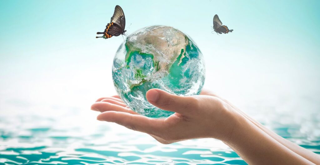 Mão segurando o planeta Terra com borboletas ao redor, simbolizando a bioeconomia e a sustentabilidade na Amazônia.