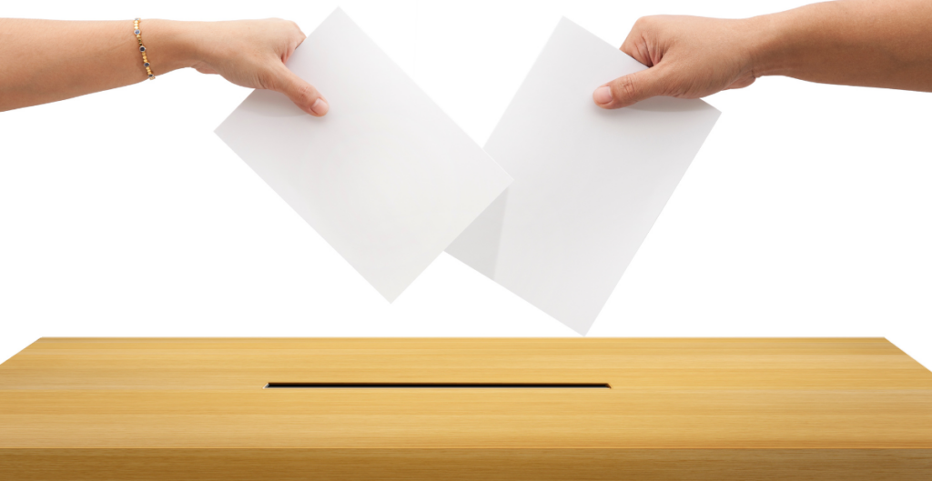 Duas pessoas inserindo cédulas de votação em uma urna de madeira.