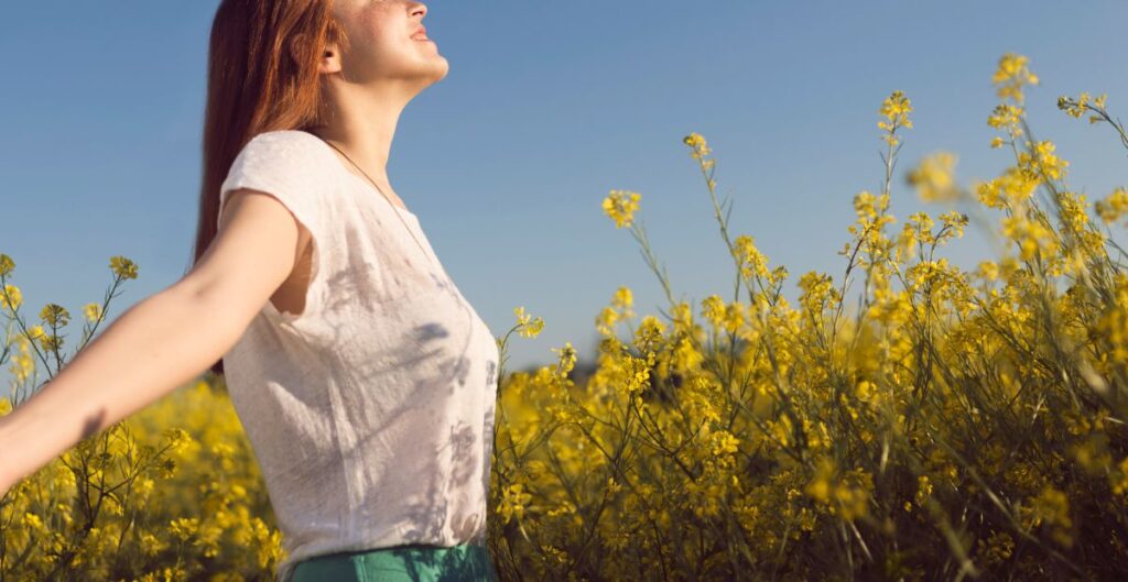 Mulher em campo de flores amarelas se conectando com a natureza, representando autoconhecimento e iluminação pessoal.