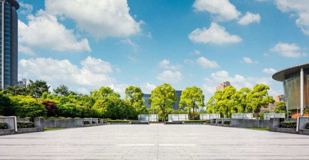 praça urbana arborizada com edifícios modernos ao fundo sob um céu azul claro.