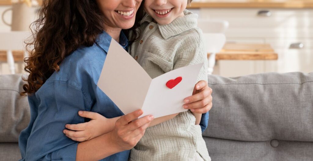 Mãe e filho compartilhando um momento afetuoso enquanto leem um cartão com coração vermelho.