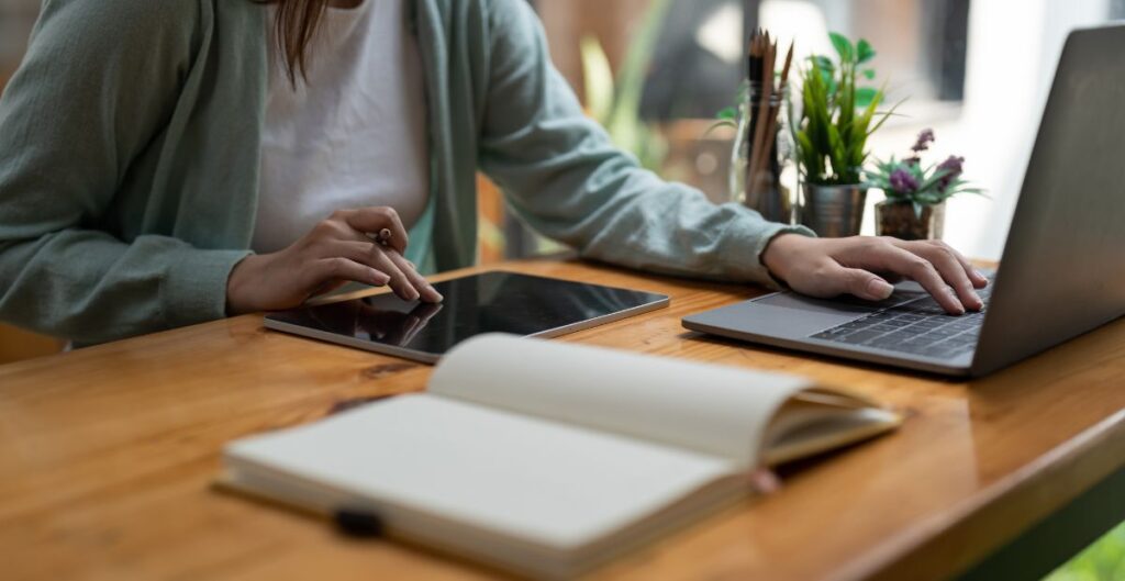 Mulher usando laptop e tablet em um ambiente de trabalho, representando o ato de empreender e inovar.