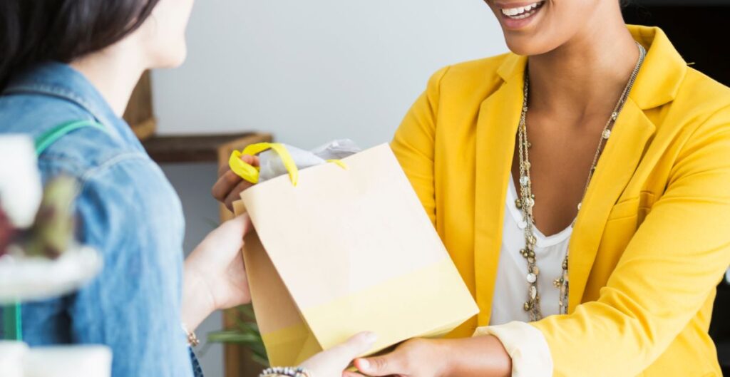 Cliente feliz recebendo pacote de presente de vendedora sorridente.