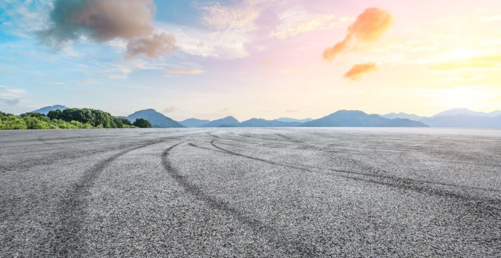 "Pista com marcas de pneus ao amanhecer, cercada por montanhas e céu colorido, simbolizando reflexão e autoconhecimento."