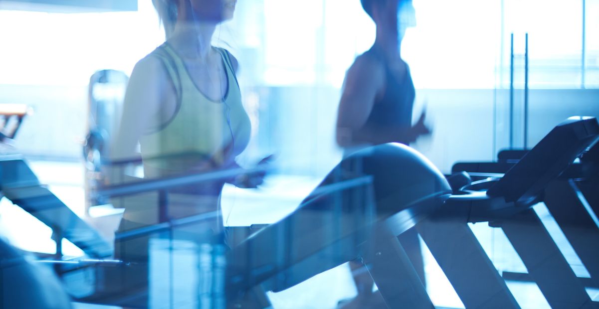 Duas pessoas correndo em esteiras em uma academia moderna, refletindo a integração entre atividade física e tecnologia no monitoramento de desempenho esportivo.Duas pessoas correndo em esteiras em uma academia moderna, refletindo a integração entre atividade física e tecnologia no monitoramento de desempenho esportivo.