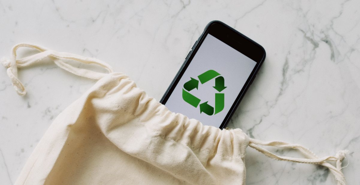 "Smartphone com símbolo de reciclagem saindo de saco de algodão, representando consumo sustentável e consciente."