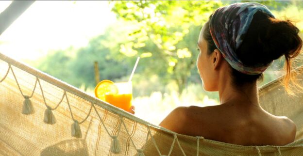 Mulher relaxando em rede ao ar livre com suco natural, representando a desaceleração do ritmo empreendedor