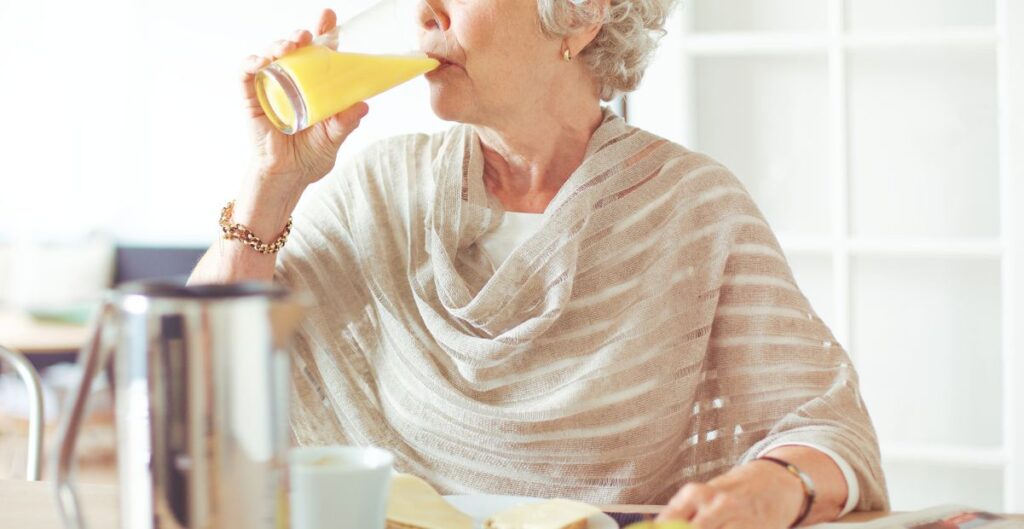 Mulher idosa elegante tomando suco de laranja durante o café da manhã.