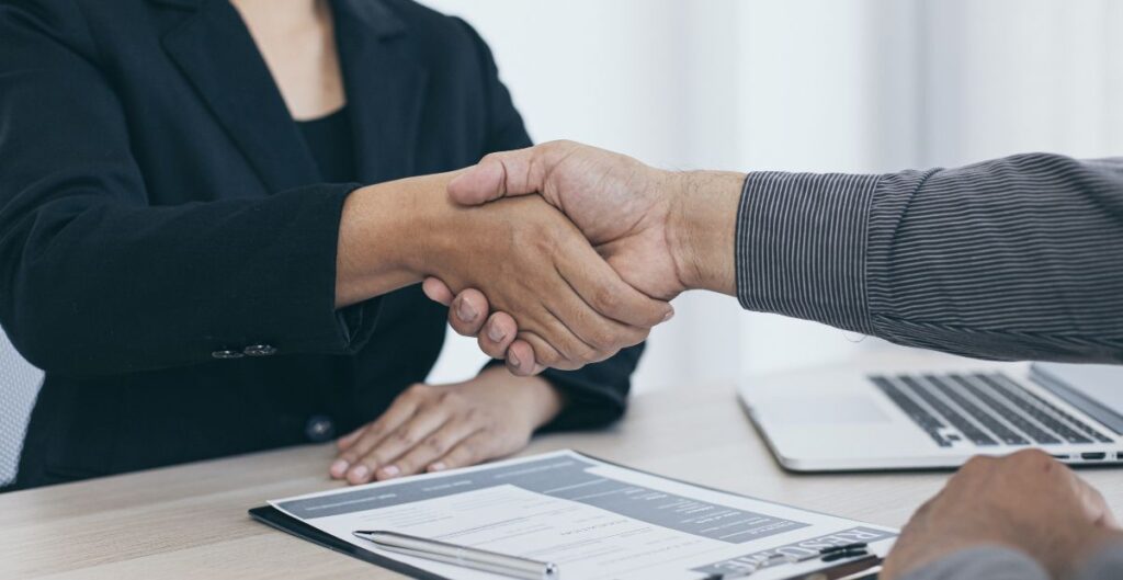 Aperto de mãos entre recrutador e candidato, simbolizando contratação de profissionais alinhados às novas tecnologias e tendências do mercado.