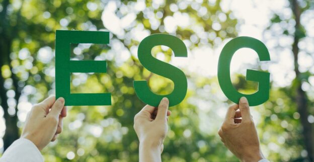 Mãos segurando letras ESG em ambiente verde representando sustentabilidade e governança.