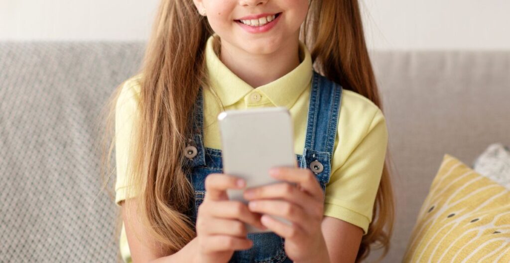 Criança sorridente usando celular sentada no sofá.