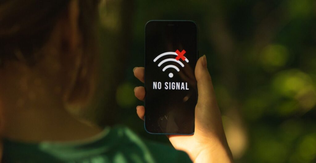 Pessoa segurando celular com aviso de “sem sinal” em ambiente externo.