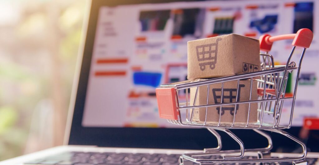 Carrinho de compras com caixas em frente a notebook simbolizando consumo digital e futuro do e-commerce