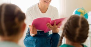 Mulher lendo livro rosa para crianças em ambiente educativo