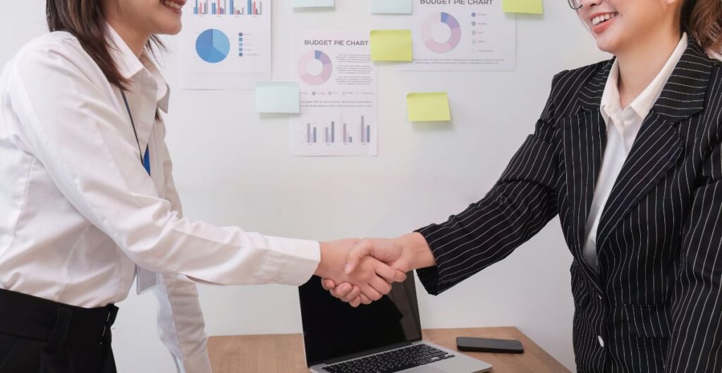 Duas mulheres cumprimentando-se com aperto de mão em ambiente corporativo.