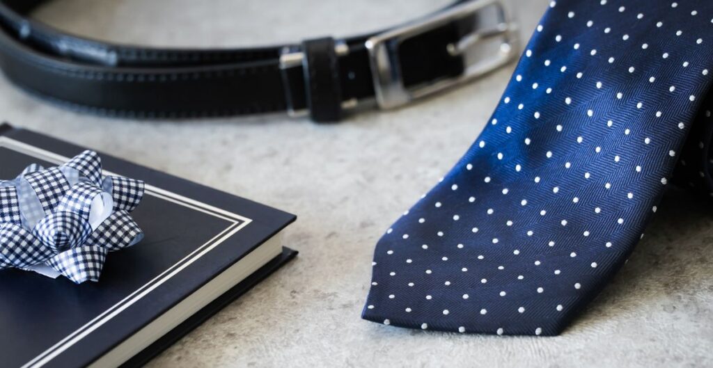 Gravata azul marinho de poá, cinto de couro preto e presente embalado.