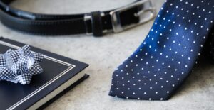 Gravata azul marinho de poá, cinto de couro preto e presente embalado.