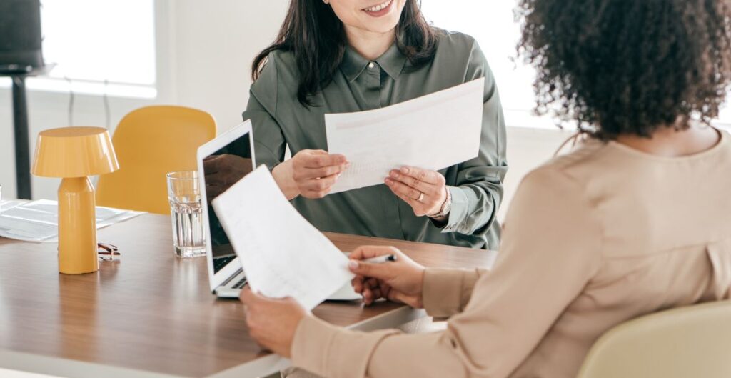 Duas mulheres em reunião analisando documentos e laptop, simbolizando as transformações do mercado de trabalho com a digitalização e a inteligência artificial.