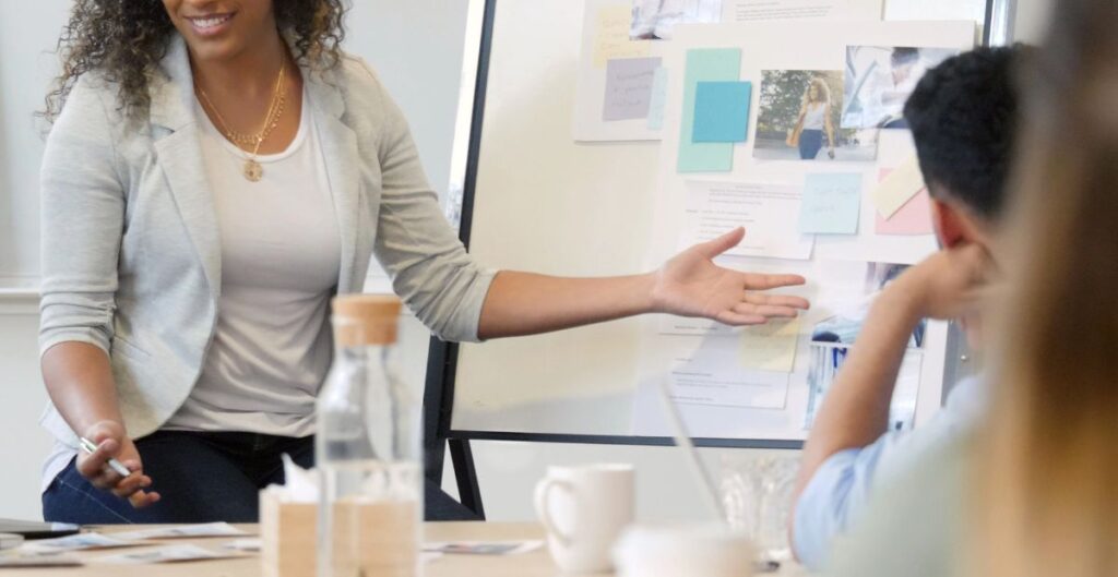 Mulher apresentando ideias em reunião de trabalho com colegas, destacando a importância da comunicação clara e objetiva no ambiente corporativo